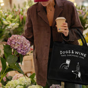 Person holding a coffee cup and a tote bag with floral arrangement in the background